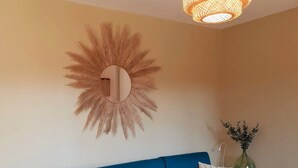 Ein modernes Wohnzimmer mit einem blauen Ecksofa, einem runden Spiegel, einem kleinen weißen Tisch und einer Pendelleuchte.