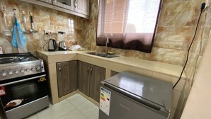 A kitchen with a gas stove, oven, refrigerator, and a window with blinds. - Modern Apartment in Kampala With Unlimited Wifi (Kampala)