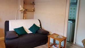 Un salon comprenant un canapé, une petite table d’appoint en bois et une étagère murale ornée d’objets décoratifs.
