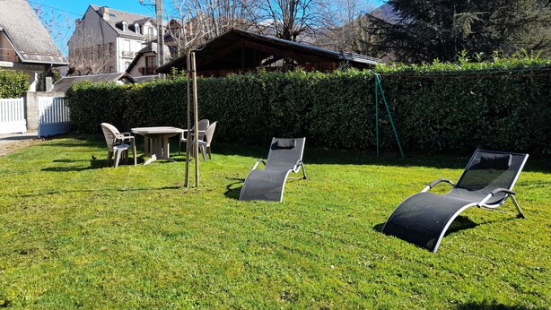 Un jardin avec une pergola en bois, deux fauteuils de jardin, une table et des chaises.