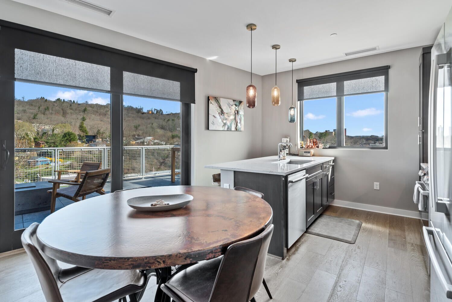 A modern kitchen with a large island, pendant lighting, and a view of a hilly landscape.