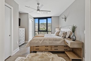 Relax in a serene bedroom with a large bed, nightstand, and ceiling fan, offering a stunning mountain view.