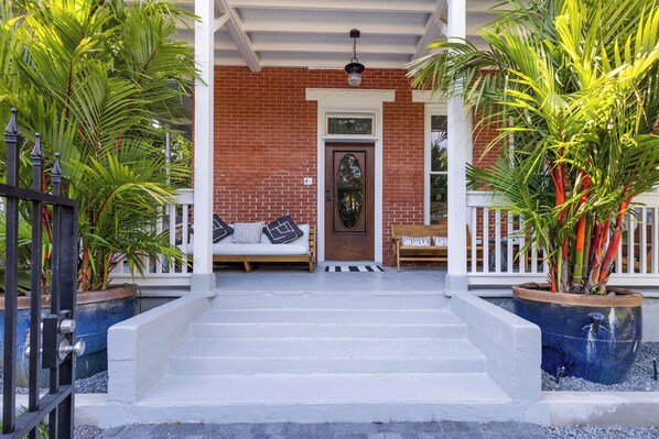 A porch with steps leading to a door, a bench, and potted plants.