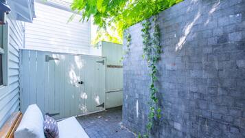 A small outdoor seating area with a bench and cushions, a stone wall, and a wooden gate.