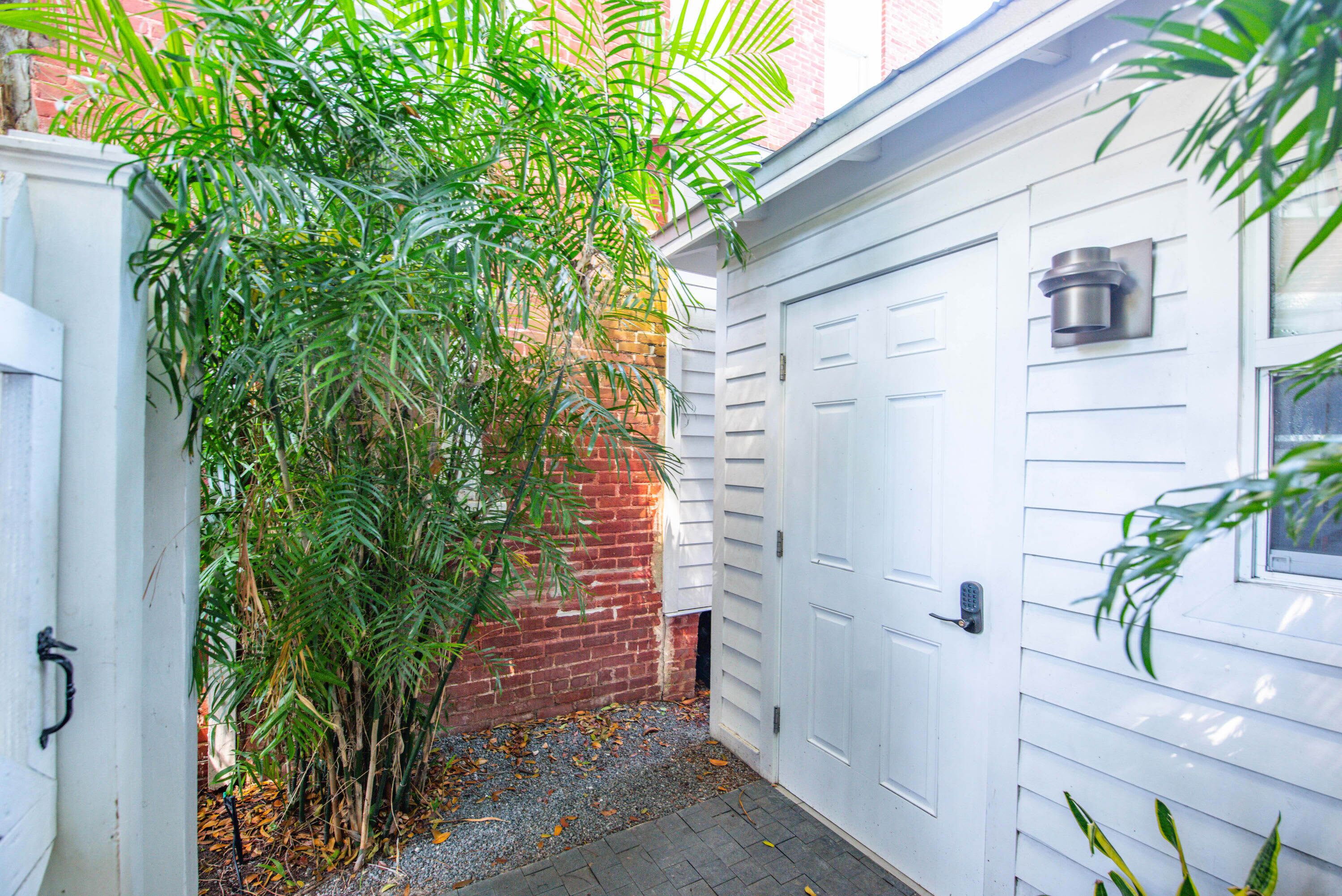 A white garage door, a brick wall, and a small garden area with a tree and gravel path.