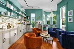 A modern kitchen with white cabinets, a marble countertop, and a dining area with orange chairs and a blue sofa set.
