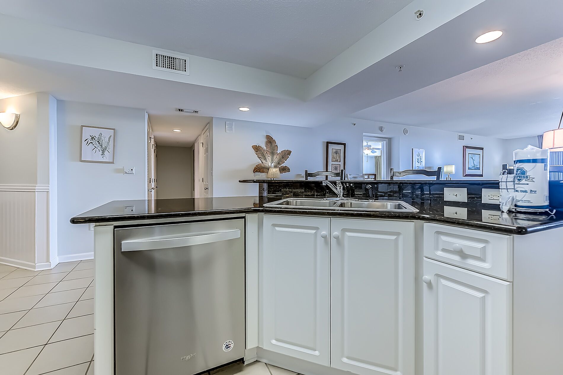 A modern kitchen with white cabinetry, a black countertop, and a built-in dishwasher.