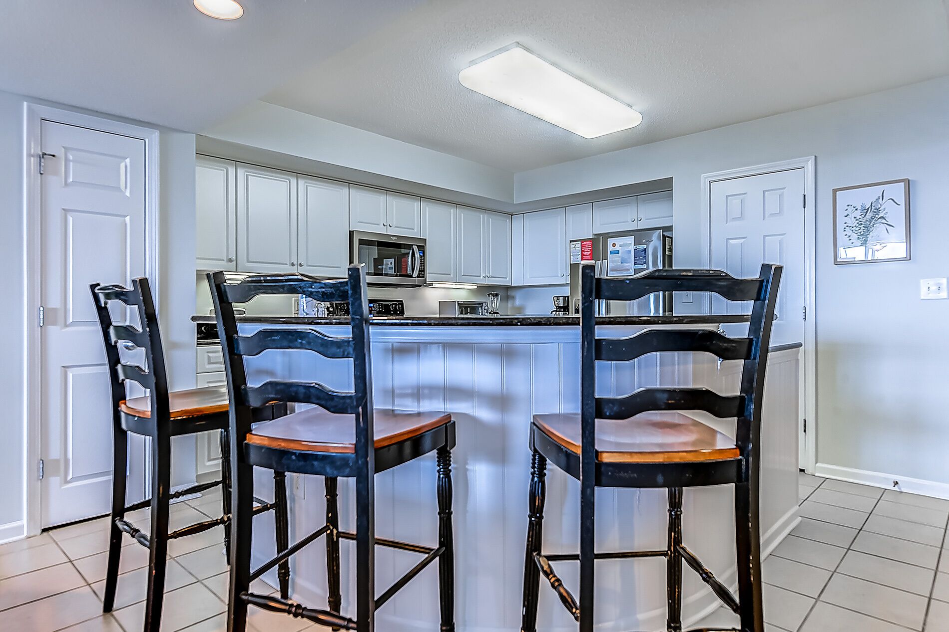 A kitchen with white cabinets, a central island, and three bar stools.