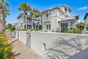 A modern two-story house with a balcony, a gated entrance, and a paved walkway.