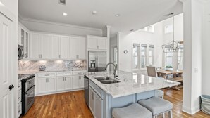 Una cocina moderna con armarios blancos, encimera de mármol y una isla central con taburetes de bar.