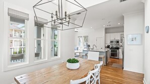 Una cocina amplia con armarios blancos, una mesa de comedor de madera y una lámpara de techo moderna.