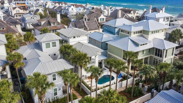 Zona residencial costera con casas de tejados a dos aguas y una piscina rodeada de palmeras.