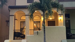 Um edifício de dois andares com fachada bege, janelas em arco e uma palmeira em primeiro plano.
