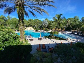A resort pool area with lounge chairs and umbrellas, surrounded by palm trees and greenery. -  Resort home, walk to it all, swim in two lush resort pools. (Naples)