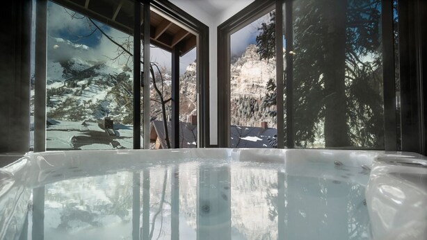 A hot tub with a view of snow-covered mountains and trees through large windows.
