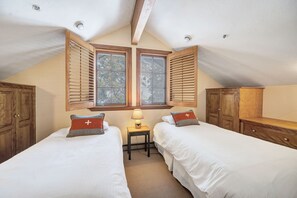 A bedroom with two beds, wooden wardrobes, a small table with a lamp, and a window with shutters. - Ski in/Ski Out to Snowbird in this Beautiful Unit with Hot Tub and Fireplace (Alta)