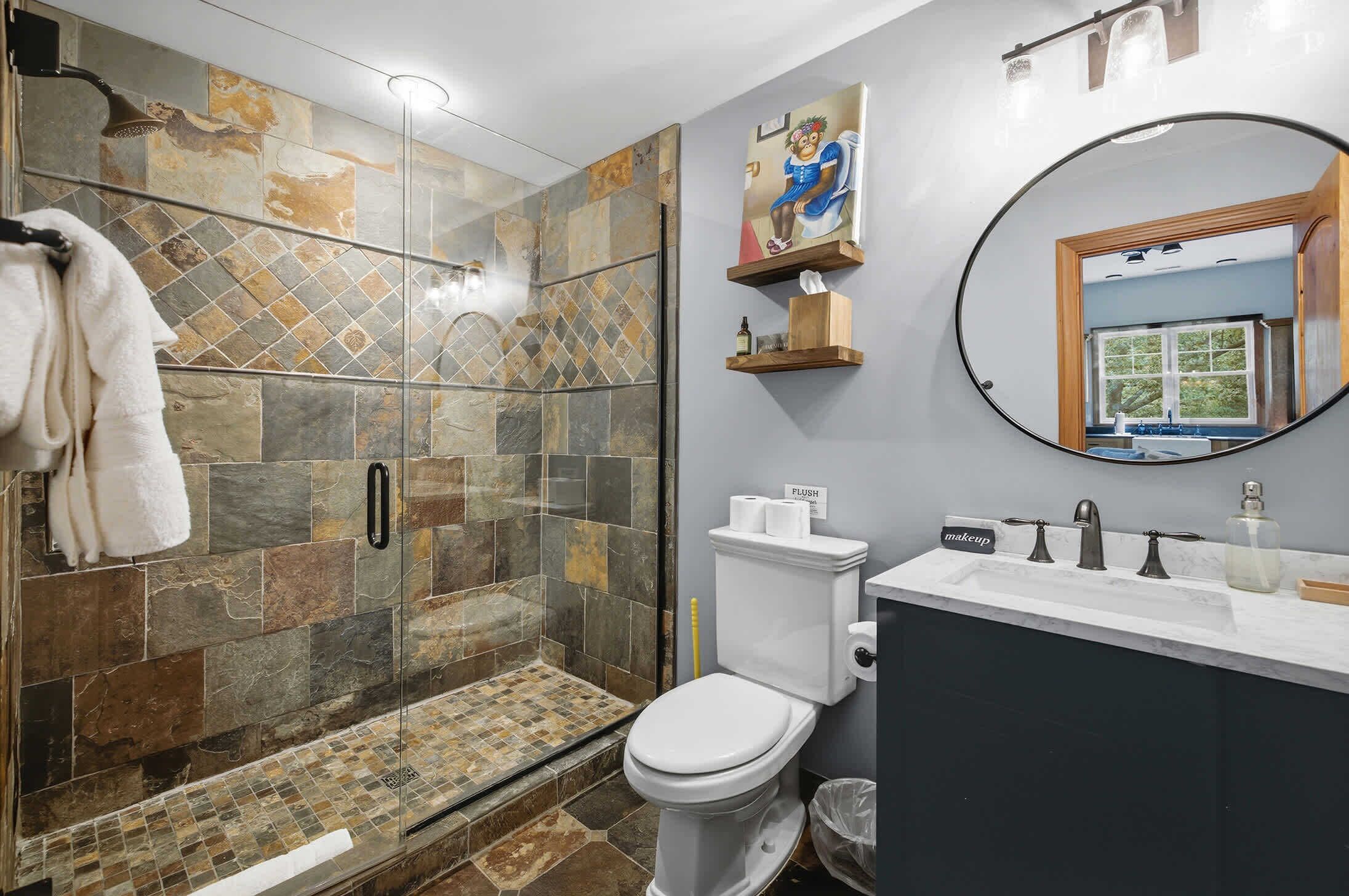Een badkamer met een douche met glazen wand, toilet, wastafel met spiegel en een handdoekhouder.
