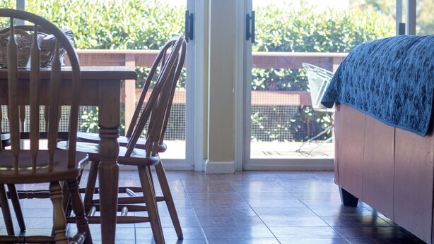 Une pièce avec une table et des chaises en bois, un canapé et, à travers une porte vitrée, une vue sur un balcon agrémenté de verdure.