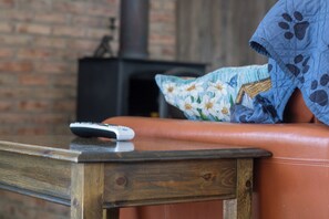 A remote control on a wooden table, a leather couch with a floral pillow, and a brick wall in the background.