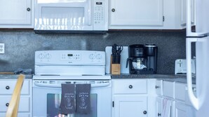 Une cuisine avec des meubles blancs, un four à micro-ondes, une cuisinière, une machine à café et un grille-pain.
