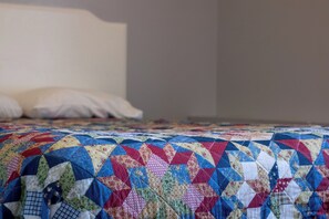 A bed with a colorful quilt and a plain headboard.