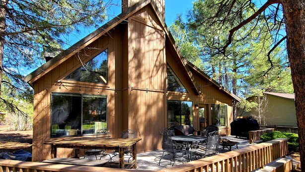 Una cabaña de madera con terraza, ventanas amplias y mobiliario exterior.