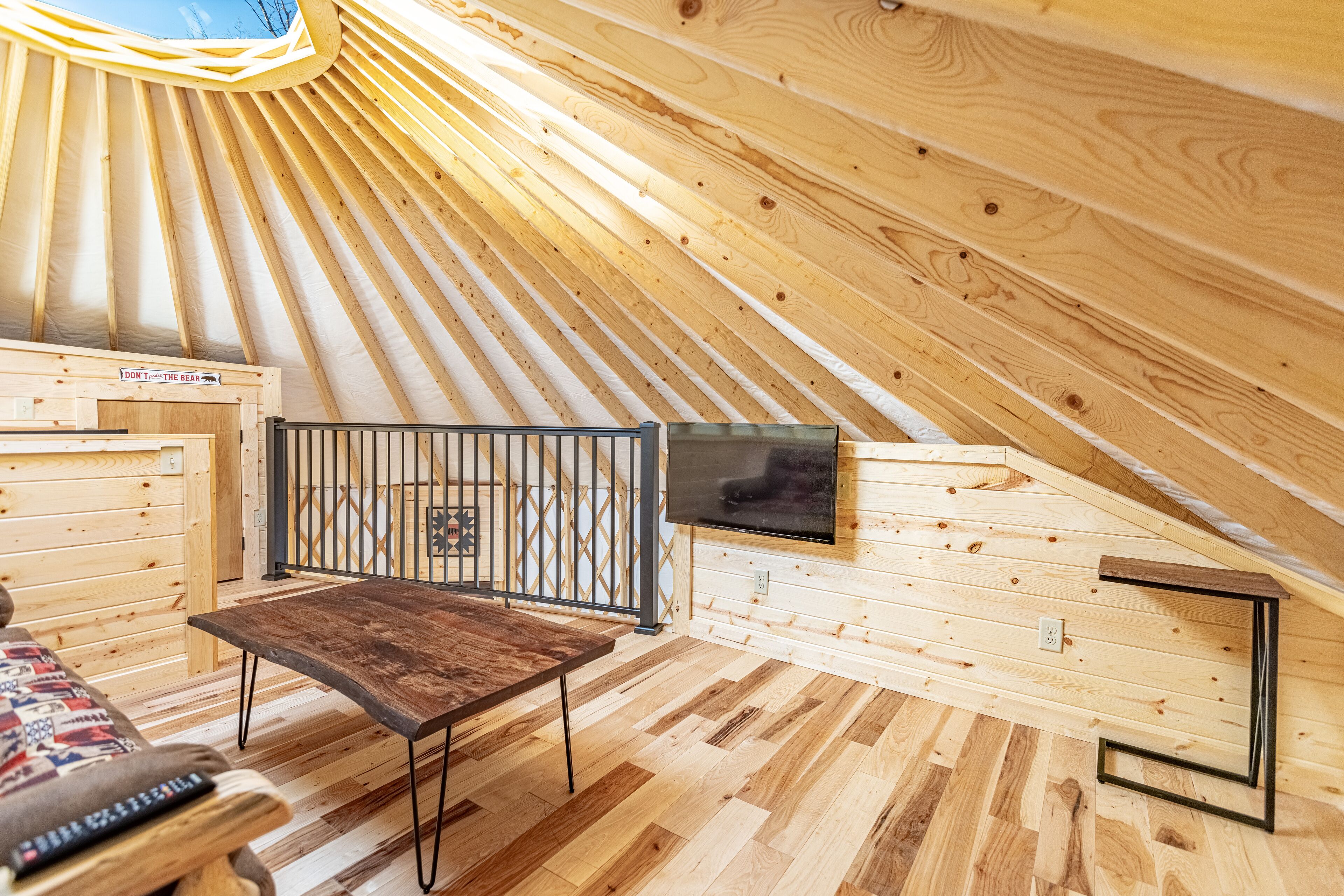 A wooden interior with a sloped ceiling, a bench, a TV mounted on the wall, and a small table.