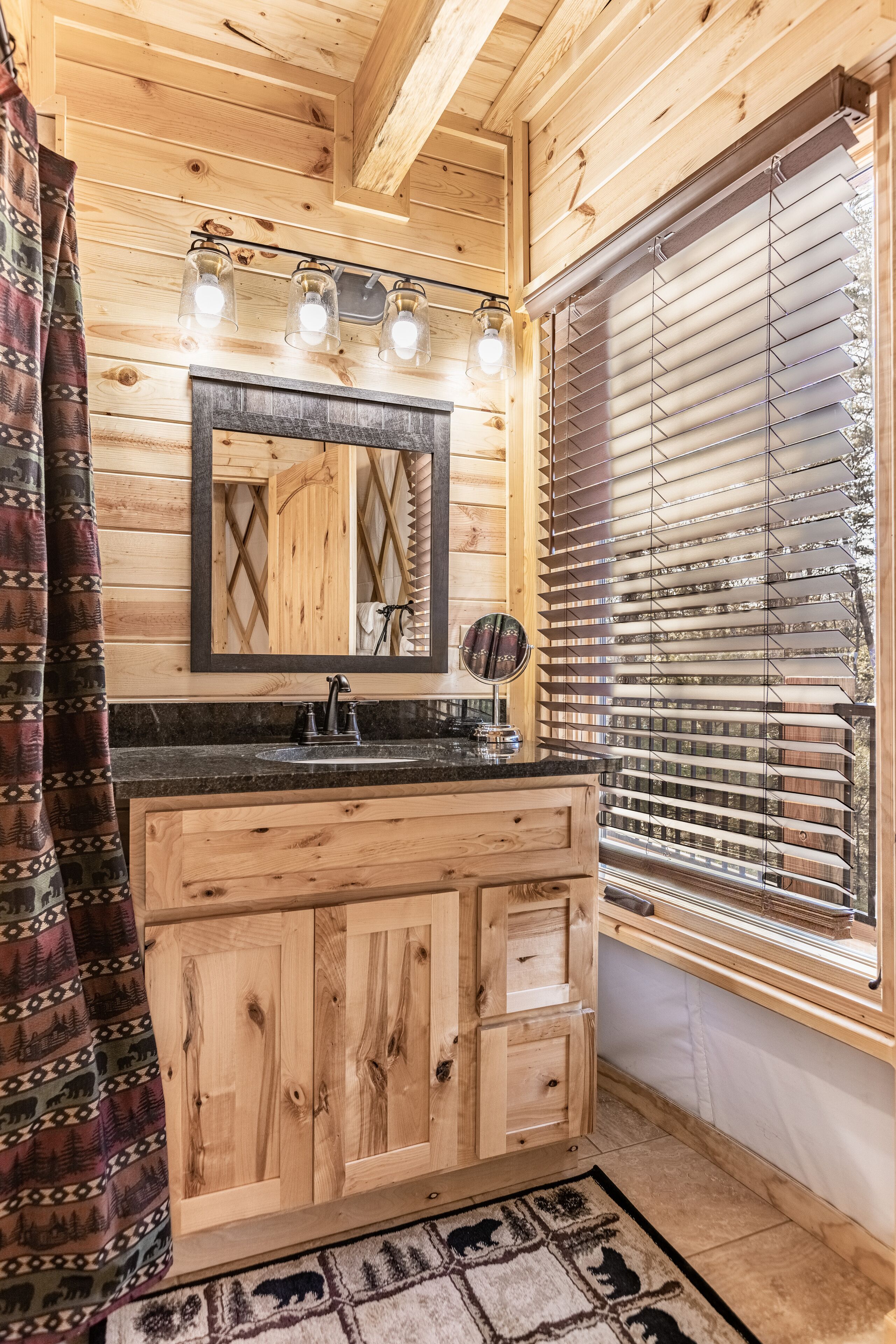 A wooden cabin bathroom with a wooden vanity, a mirror, and a window with blinds.