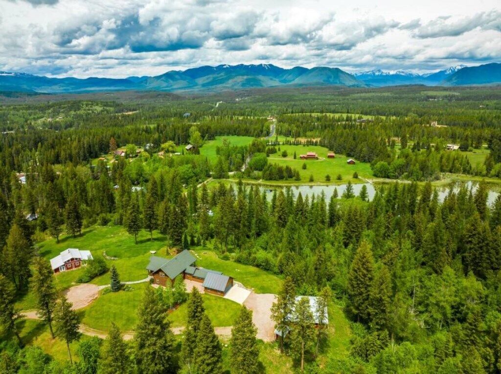 Vue aérienne d’une propriété rurale avec un grand lac, des zones boisées et des montagnes en arrière-plan.