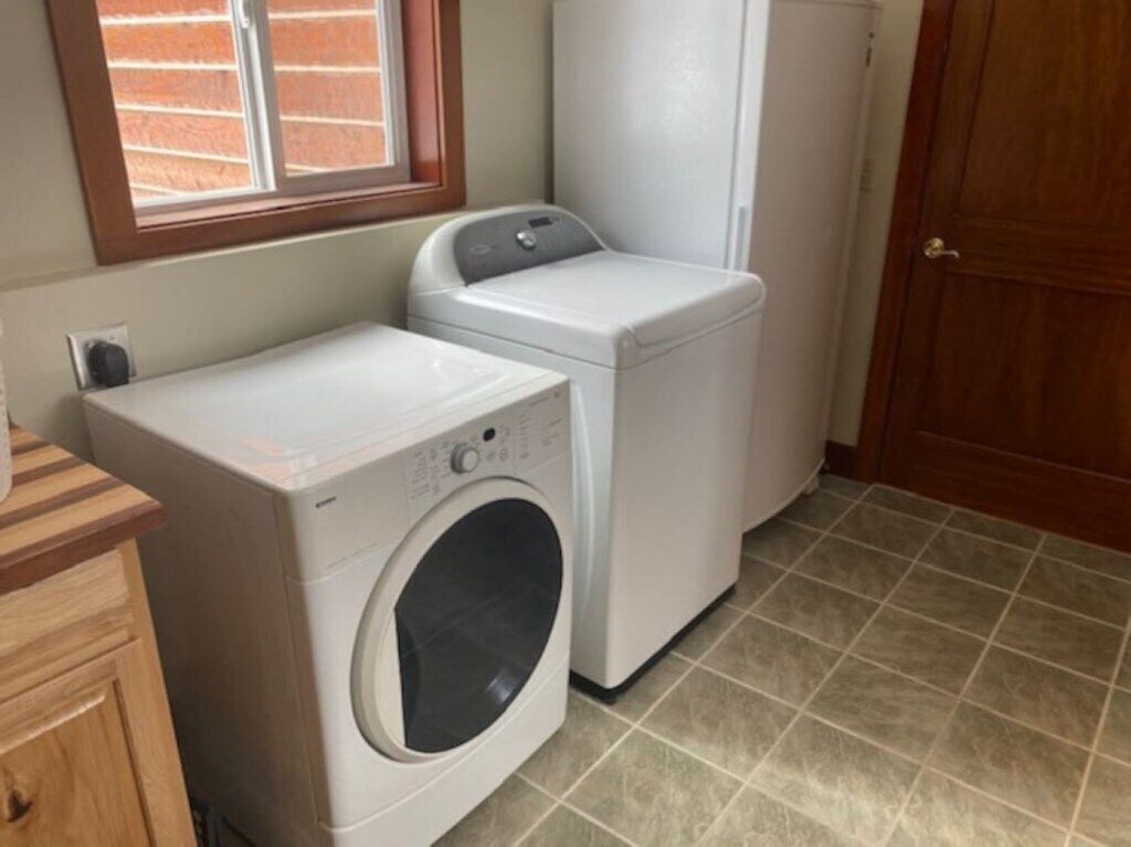 A laundry room with a front-loading washer and dryer, wooden cabinets, a tiled floor, and a door.