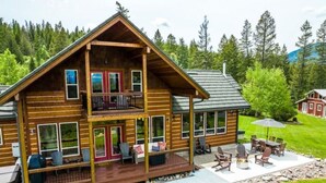 A two-story log cabin with a balcony, outdoor seating area, and a stone pathway leading to the entrance.