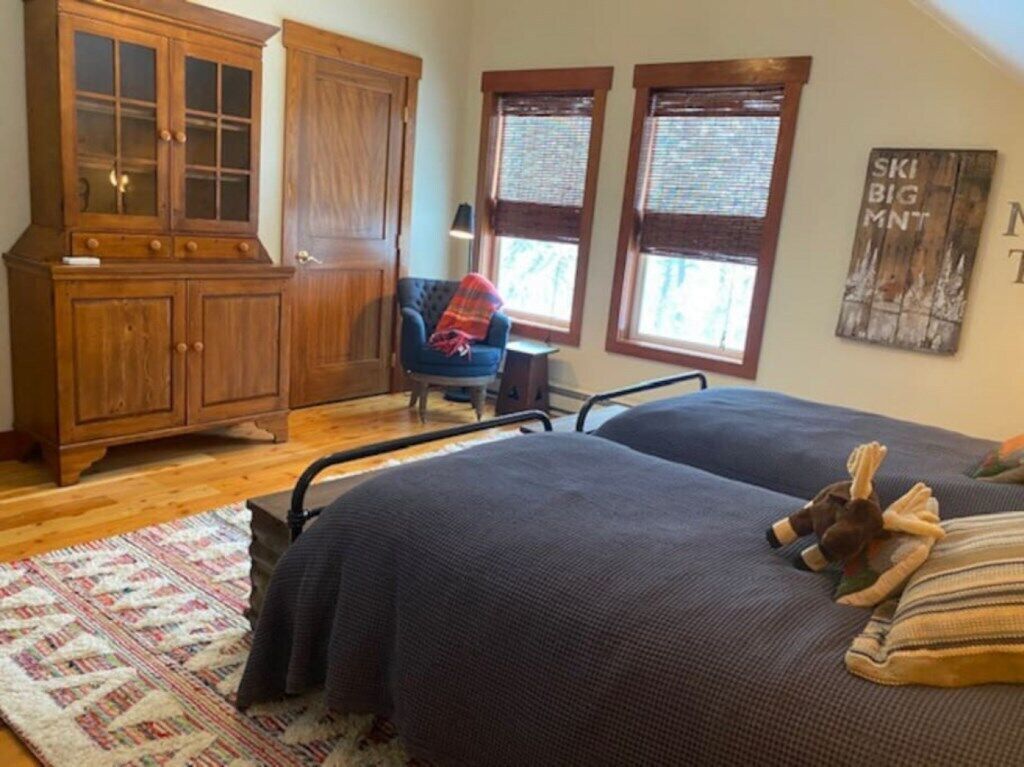 Un dormitorio con una cama grande, una silla, un armario de madera y dos ventanas con persianas.