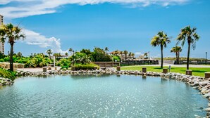 A clear pool surrounded by rocks and palm trees, with a view of buildings and a clear sky. - Romantic Getaway II w/ WiFi in Oceanfront Gated Resort - 1 Bedroom Lodge (Myrtle Beach)
