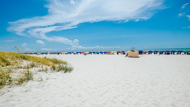 A beach with white sand and a clear blue sky. There are colorful umbrellas and beach chairs lined up along the shore. - Romantic Getaway II w/ WiFi in Oceanfront Gated Resort - 1 Bedroom Lodge (Myrtle Beach)