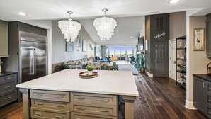 Une cuisine spacieuse dotée d’un grand îlot central, d’appareils électroménagers en acier inoxydable et d’un lustre moderne.