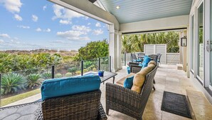 Une terrasse couverte, meublée avec des meubles en osier, dotée d’un ventilateur de plafond et offrant une vue sur le paysage.