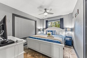 A bedroom with a bed, bedside tables, a ceiling fan, and a window with curtains.