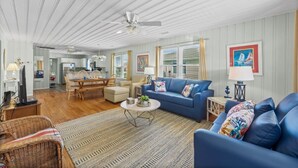 A spacious living room with a blue sofa, a dining table, and a kitchen in the background.
