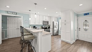A modern kitchen with white cabinets, a central island with bar stools, a microwave, and a refrigerator. - Enjoy a Luxury Rental at Salt Life - Private Pool & Ocean View Balcony (North Myrtle Beach)