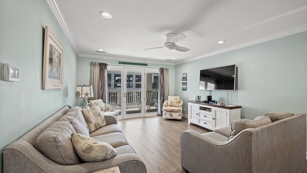 A living room with a sofa, armchair, and TV. There is a sliding glass door leading to a balcony. - Enjoy a Luxury Rental at Salt Life - Private Pool & Ocean View Balcony (North Myrtle Beach)