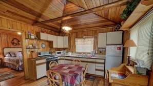 Une cuisine chaleureuse, aménagée dans le style d’un chalet, avec des murs et des planchers en bois, une table à manger avec des chaises, un fourneau, un four à micro-ondes et un réfrigérateur.