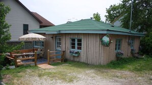 Une maison en bois avec un toit vert, une clôture en bois et un banc avec un parasol.