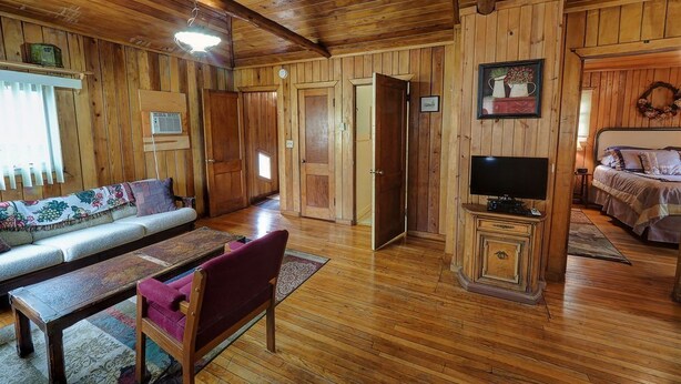 L’intérieur d’un chalet en bois, avec un canapé, un téléviseur posé sur un meuble en bois et un lit doté d’une tête de lit.