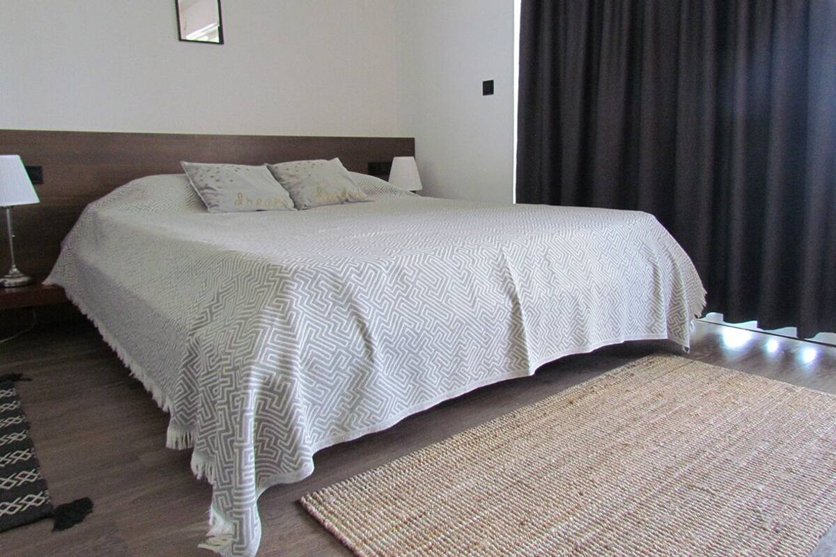 A neatly made bed with a patterned bedspread, a bedside lamp, and a dark curtain.