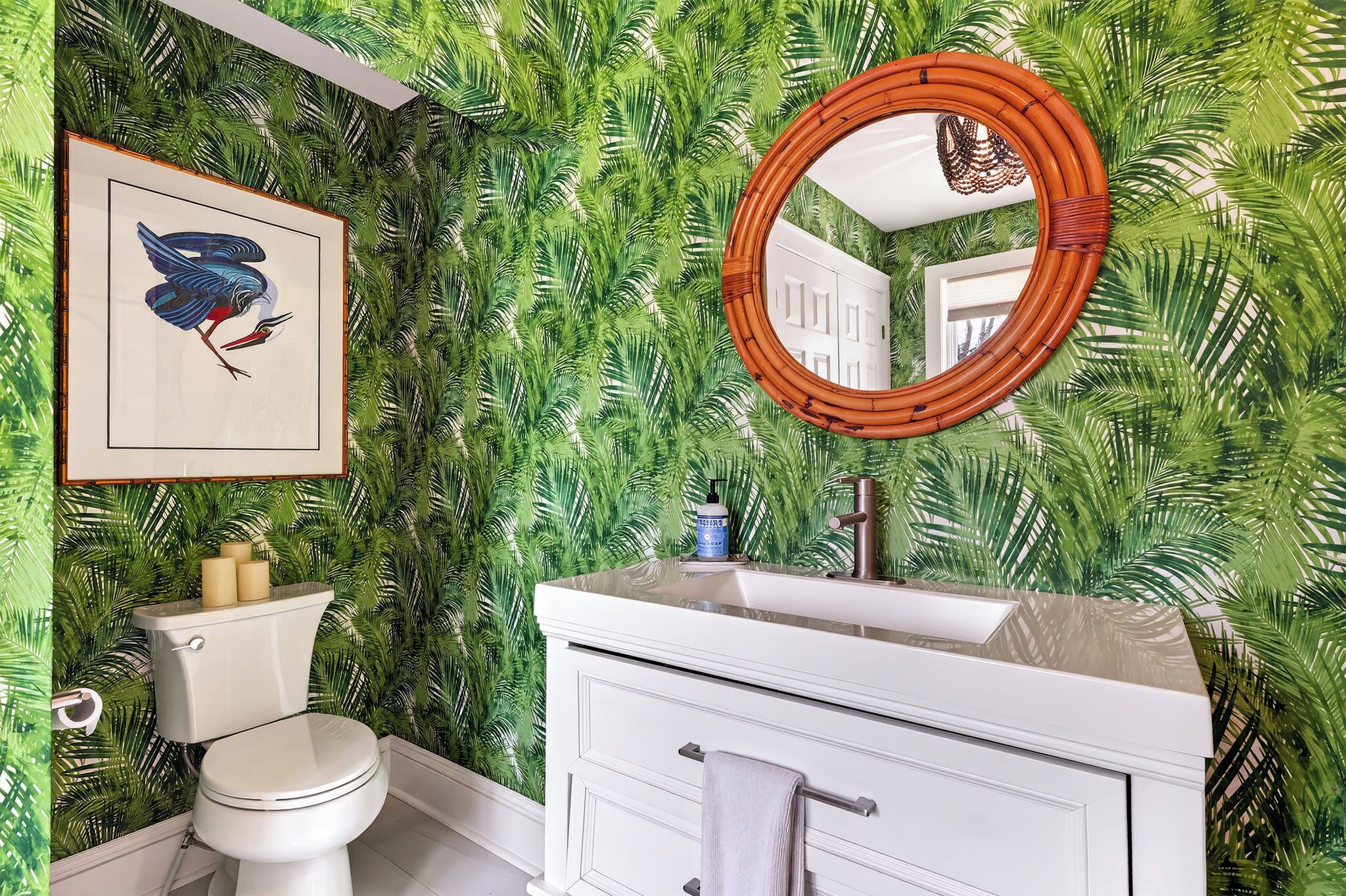 A bathroom with a toilet, sink, and mirror, surrounded by a wall with a tropical leaf pattern.