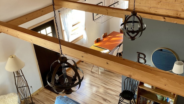 A spacious loft with a high ceiling, wooden beams, a blue sofa, a dining area, and a bookshelf.