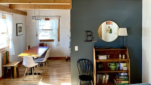 A dining area with a wooden table and chairs, a bookshelf with books and games, and a ceiling with exposed beams.