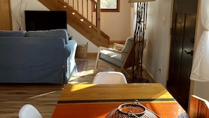 A living room with a wooden staircase, a sofa, a table with a lamp, and a door.