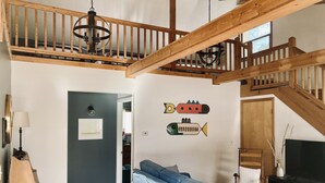 A spacious living area with a blue sofa, wooden ceiling beams, a chandelier, and a wall-mounted fish decoration.