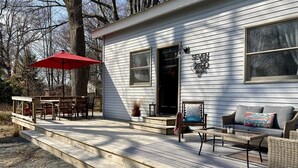 A wooden deck with outdoor furniture, a red umbrella, and a house with a large window and a door.